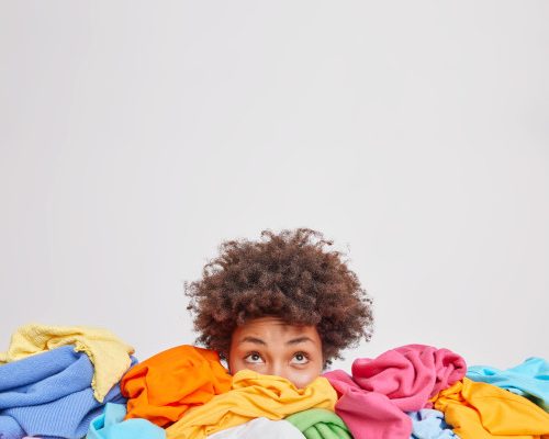 young-afro-american-woman-surrounded-by-different-colorful-clothes-sorts-out-wardrobe-focused-isolated-white-wall-blank-space-your-advertising-content-nothing-wear-concept(1)