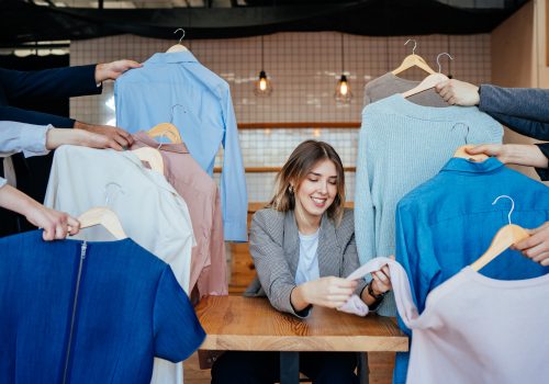 Young contemporary stylist looking through set of shirts and other casualwear choosing one for fashion shooting